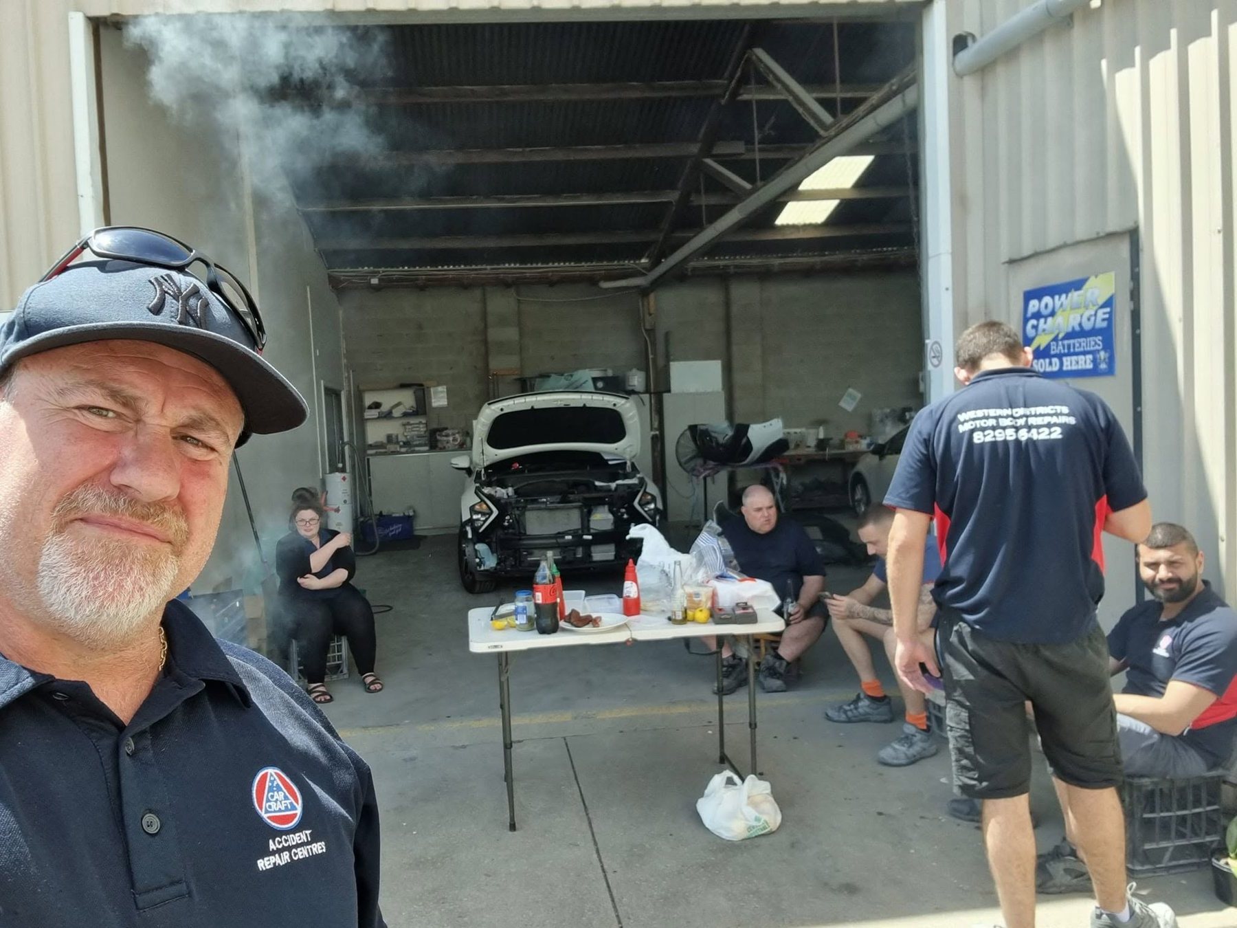 The Western Districts team having a barbecue lunch in the workshop doorway, with a car mid-repair behind them