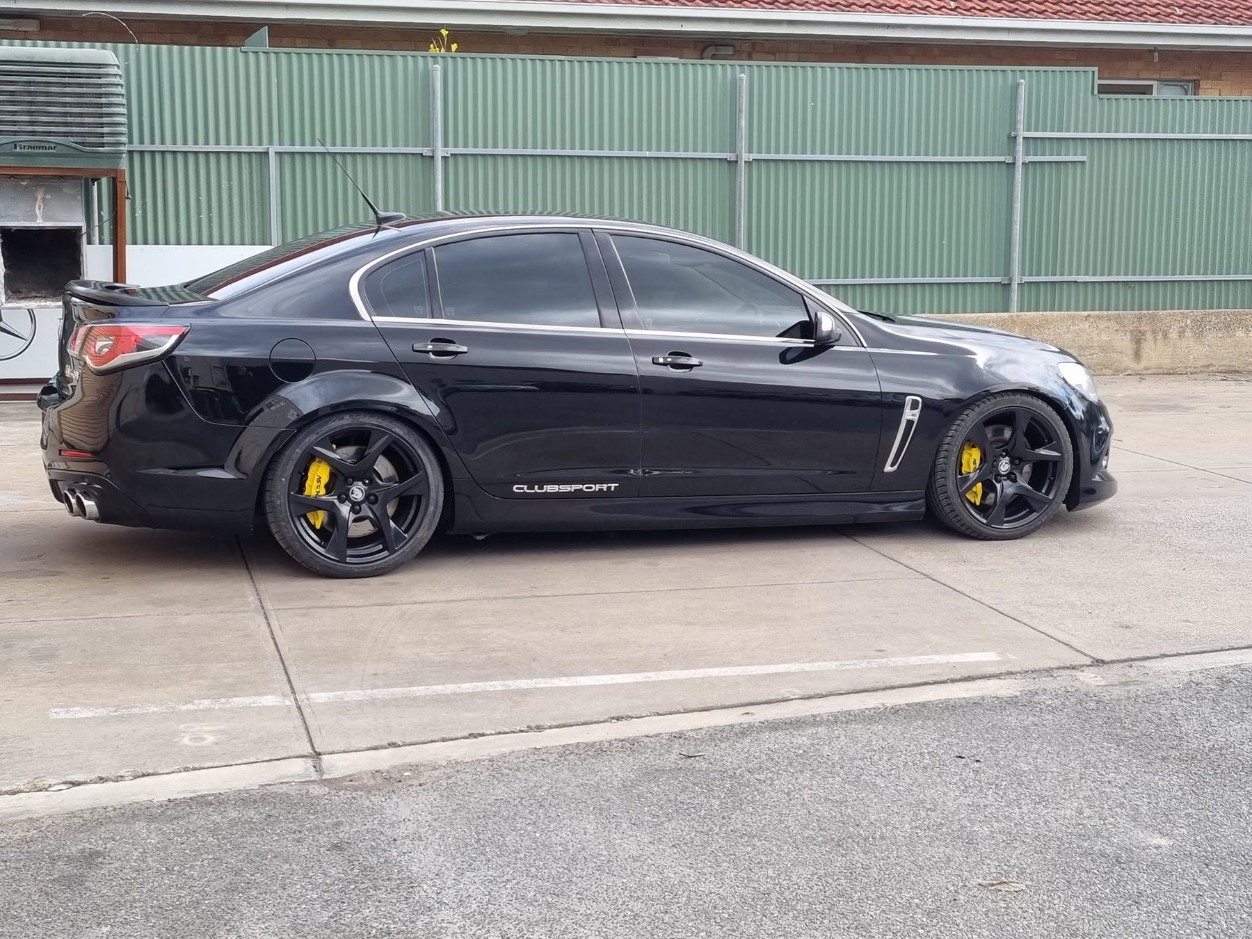 A gloss-black HSV Clubsport with yellow brake calipers, side-on in front of a green fence