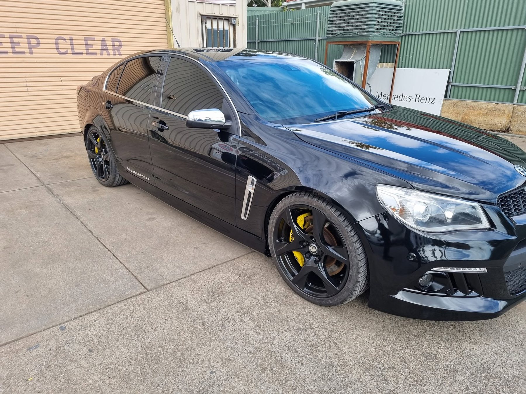 The same black HSV Clubsport from the front, its paint reflecting the sky