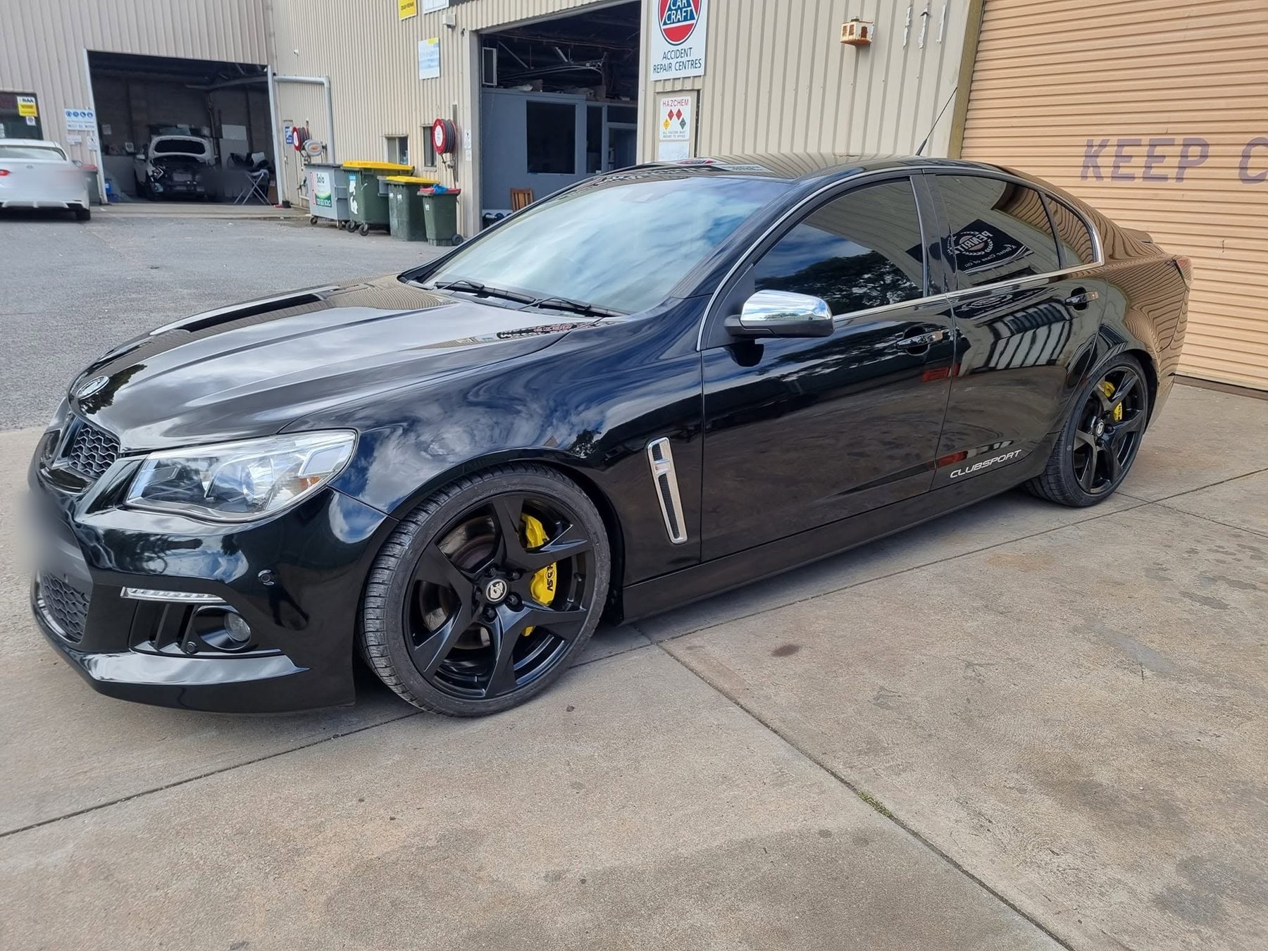 A gloss-black HSV Clubsport with yellow brake calipers parked outside the Western Districts workshop, under the CarCraft Accident Repair Centres sign